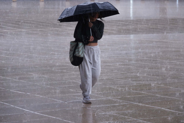 Una mujer se protege de la lluvia mientras camina por el pasillo central del Monumento a la Revolución.