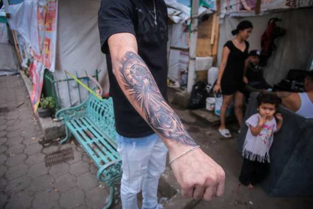 Un cliente muestra el tatuaje de un reloj, una cruz y rosas.