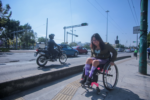 La joven se desplaza por una banqueta  con rampa para cruzar una vialidad.