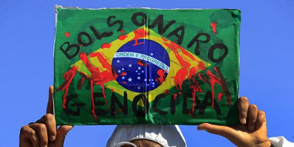En esta fotografía de archivo del 26 de mayo de 2021, un manifestante sostiene una imagen de la bandera brasileña cubierta de sangre falsa y la frase portuguesa "Genocidio de Bolsonaro" durante una protesta contra las políticas del presidente Jair Bolsonaro para combatir la pandemia de COVID-19