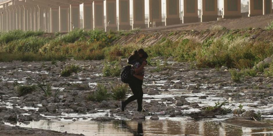 Mujer migrante que carga en hombros a su hijo cruza entre el Río Bravo, en la frontera en Juárez.
