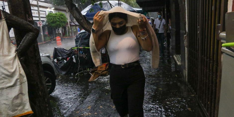 Una capitalina se cubre con su suéter mientras corre de la fuerte lluvia registrada en la alcaldía Coyoacán, en la CDMX.