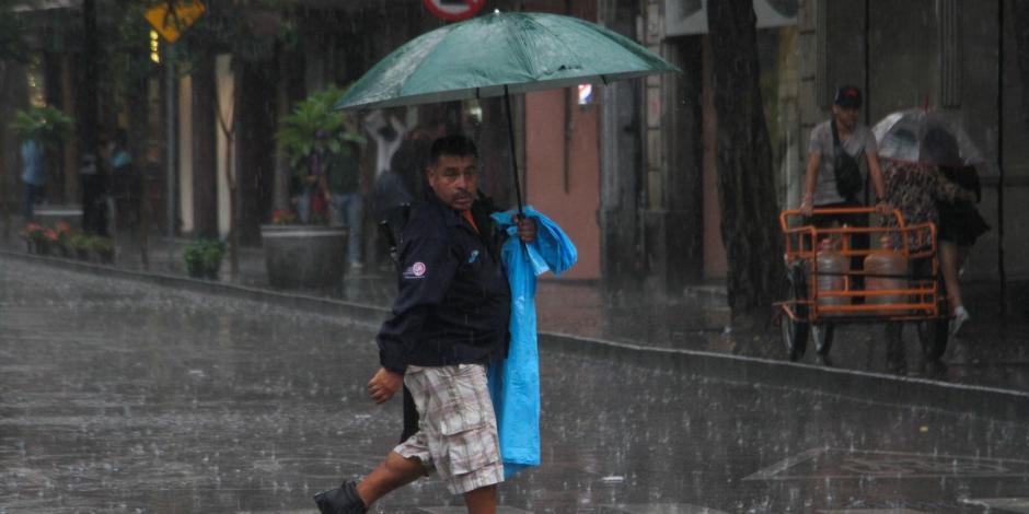 Un capitalino se camina bajo la lluvia mientras se cubre con un paraguas en calles de la CDMX.