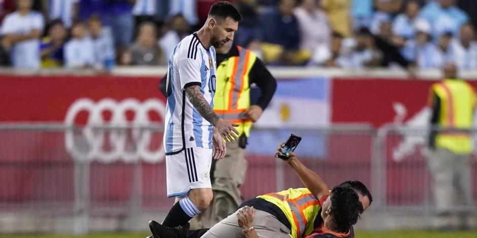 Un empleado de seguridad derriba a una persona que invadió la cancha y que intenta tomar una foto de Lionel Messi.