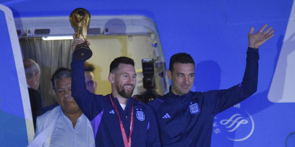 El futbolista argentino Lionel Messi sostiene el trofeo del Mundial de la FIFA a la salida de un avión junto al técnico Lionel Scaloni, en Buenos Aires, Argentina, el martes 20 de diciembre 2022