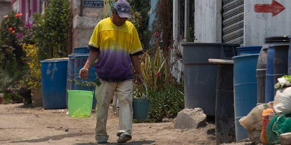 Un hombre camina por la calle cargando cubetas con agua.