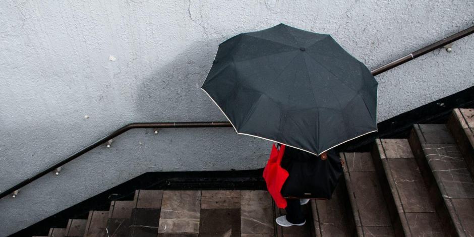 Una mujer entra al metro Centro Médico protegiéndose de la lluvia con un paragüas.