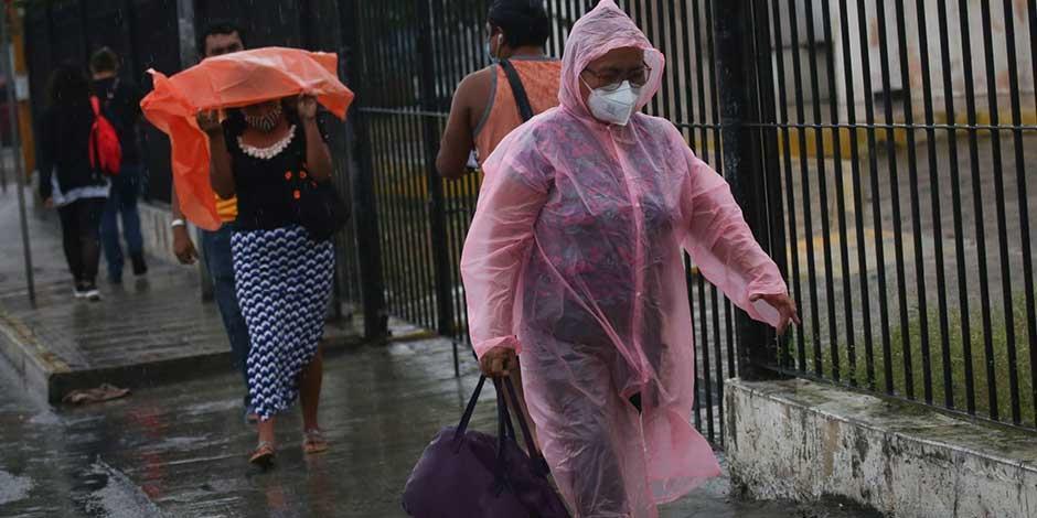 Personas camina por la calle protegiéndose con plásticos de la lluvia