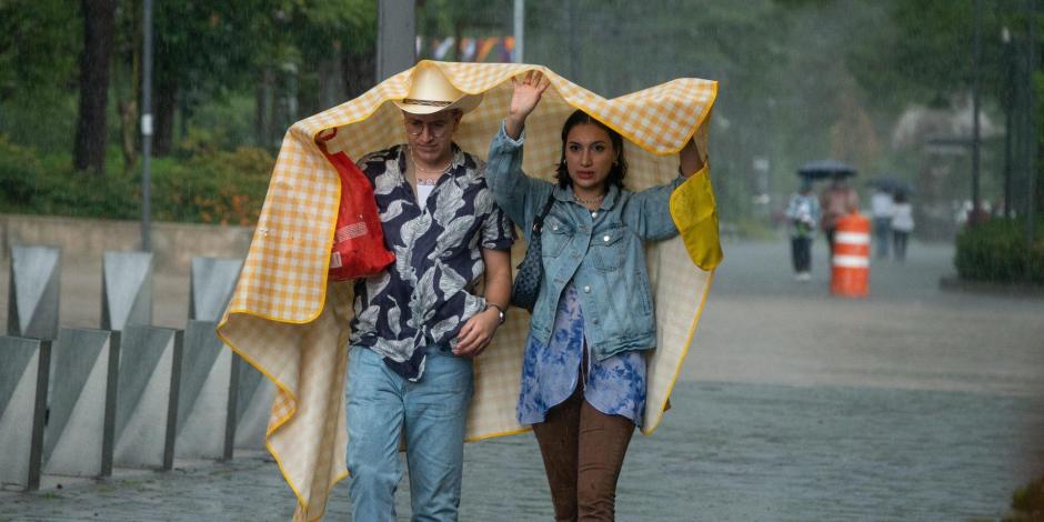 Dos personas en la calle se cubren con lo que pueden de la intensa lluvia