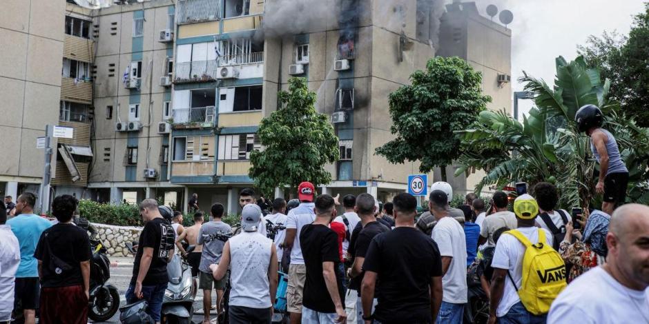 Varias personas se reúnen mientras sale humo de un edificio de apartamentos residenciales después de que un cohete, disparado desde la Franja de Gaza hacia Israel, cayera en Tel Aviv, Israel, 27 de octubre de 2023.