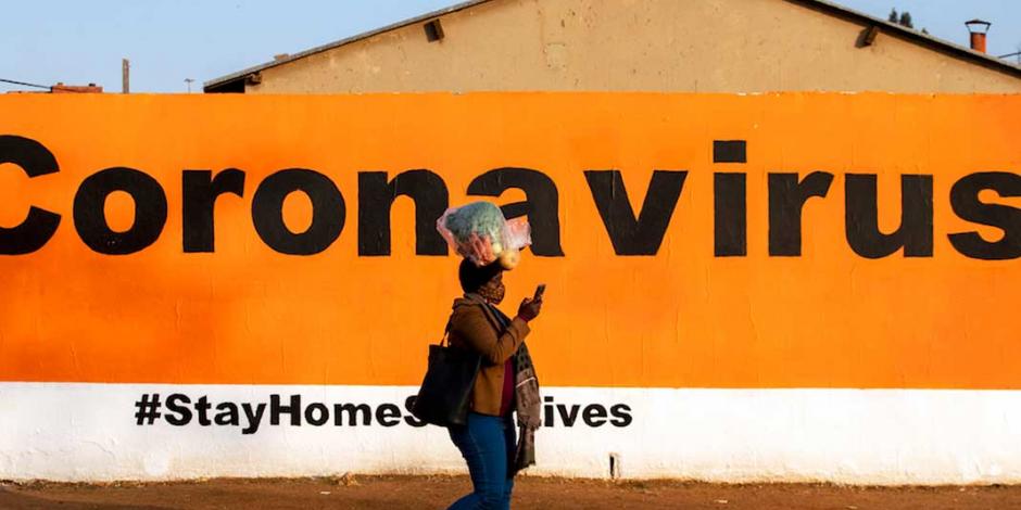Una mujer camina frente a una campaña que invita a quedarse en casa, en Johannesburgo, ayer.