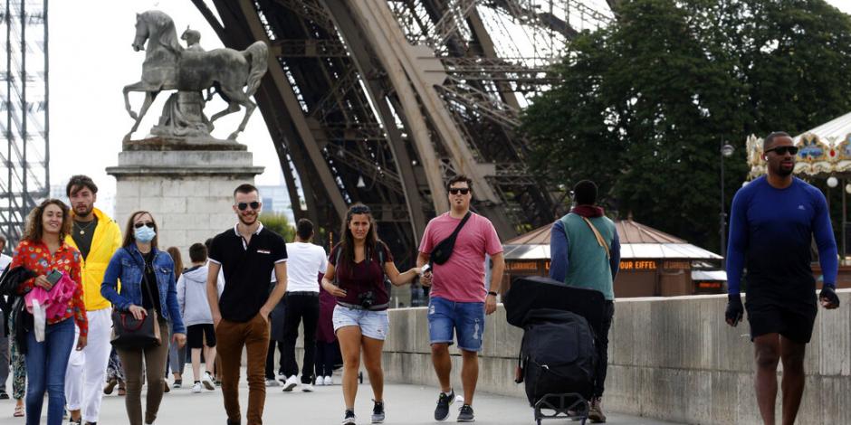 Turistas camina al lado de la Torre Eiffel en París, este domingo 26 de julio.