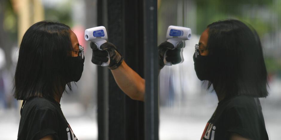 Un empleado de una tienda le toma la temperatura a una mujer como precaución contra el coronavirus el sábado 25 de julio de 2020, en Caracas, Venezuela. 