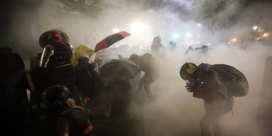 Manifestantes se cubren  con sombrillas del gas lacrimógeno, en Portland.