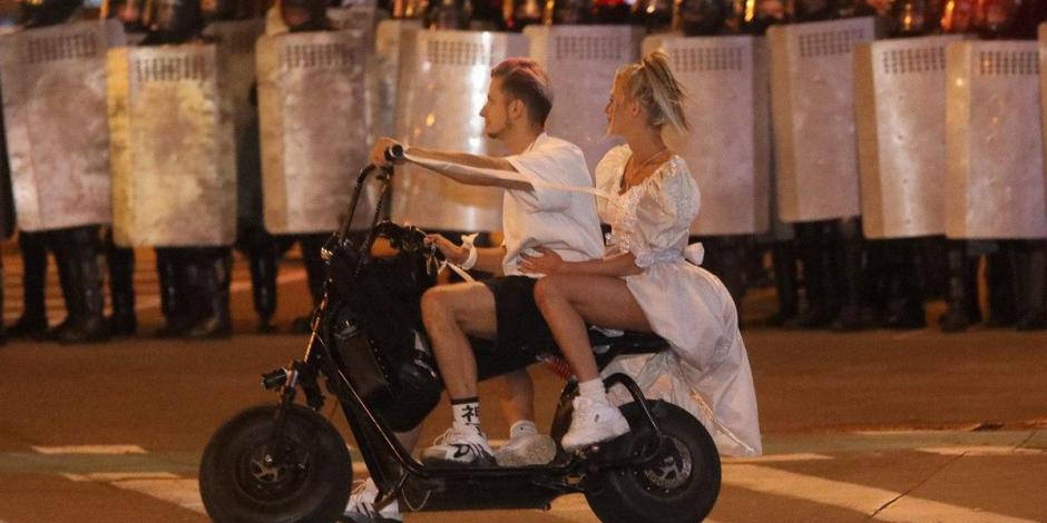 Una chica con vestido de novia pasa en una motoneta con su novio frente a un bloque de policías durante una manifestación en Minsk