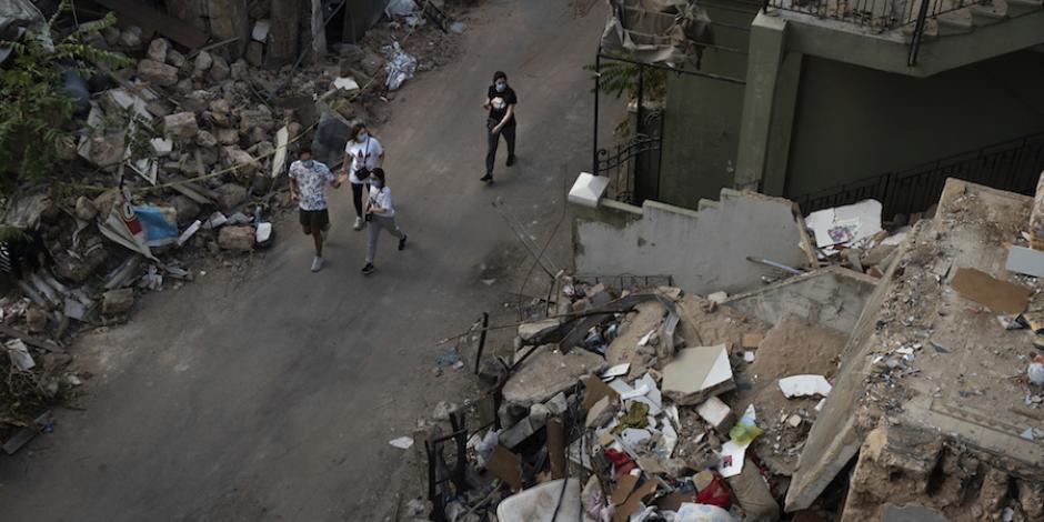Un grupo de personas camina en una calle rodeada  de los escombros que dejaron los edificios dañados, ayer.