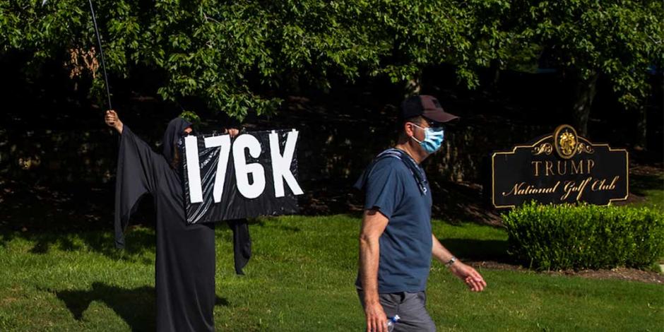 Un manifestante recuerda el número de muertes por el virus en EU, cerca del club de golf de Trump, en Virginia, ayer.