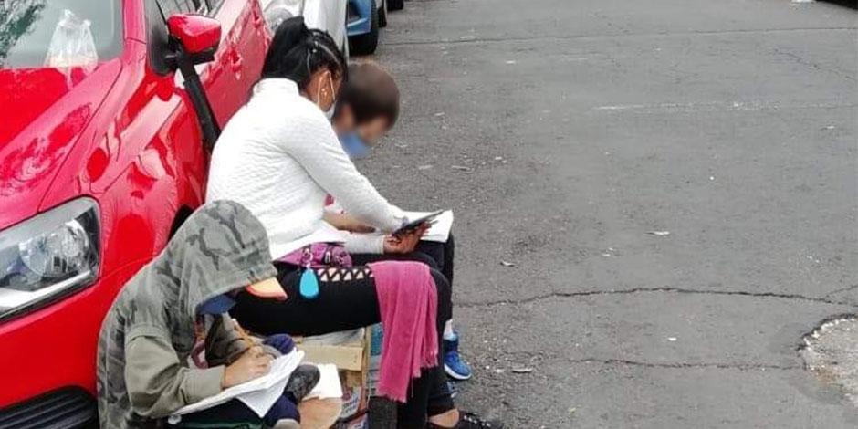 La mujer ayuda y sus dos hijos estudiando en la calle.