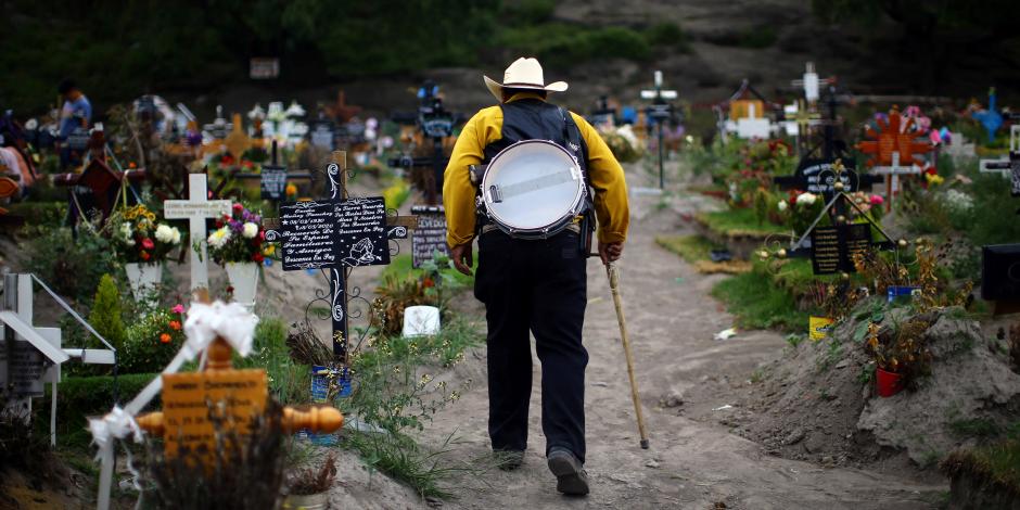 Músico camina entre tumbas en panteón en México