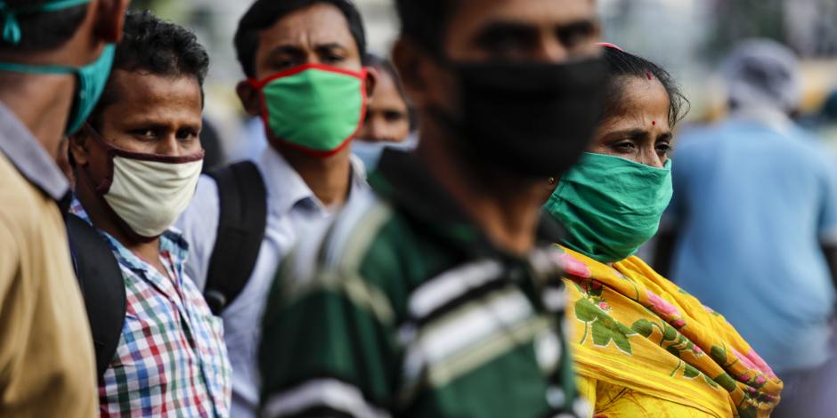 Pasajeros con mascarillas como precaución contra el coronavirus esperan a un autobús en Kolkata, India.
