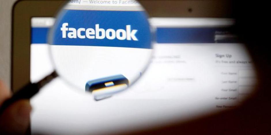 Logo de Facebook en una pantalla de computador visto a través de una lupa sostenida por una mujer.