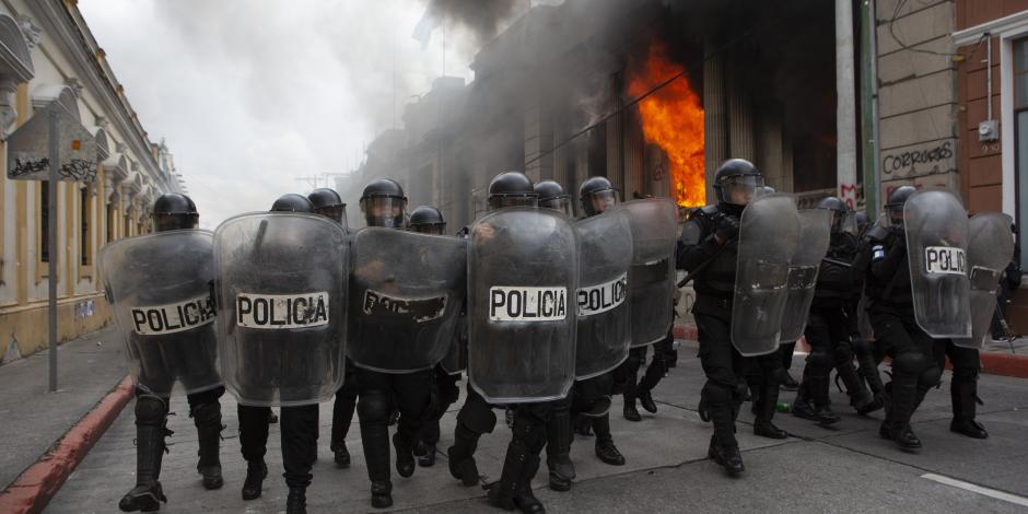 La policía antidisturbios forma un cordón mientras las llamas salen disparadas desde el edificio del Congreso después de que manifestantes incendiaran parte del edificio, en Guatemala, ayer.