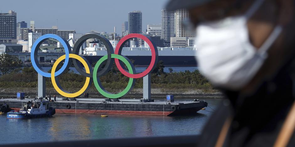 Un hombre con cubrebocas pasa frente a los anillos olímpicos en Tokio el e de diciembre de 2020.