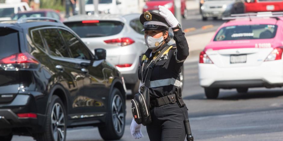 Una mujer policía con cubrebocas agiliza el tránsito en el cruce de Insurgentes y Reforma.
