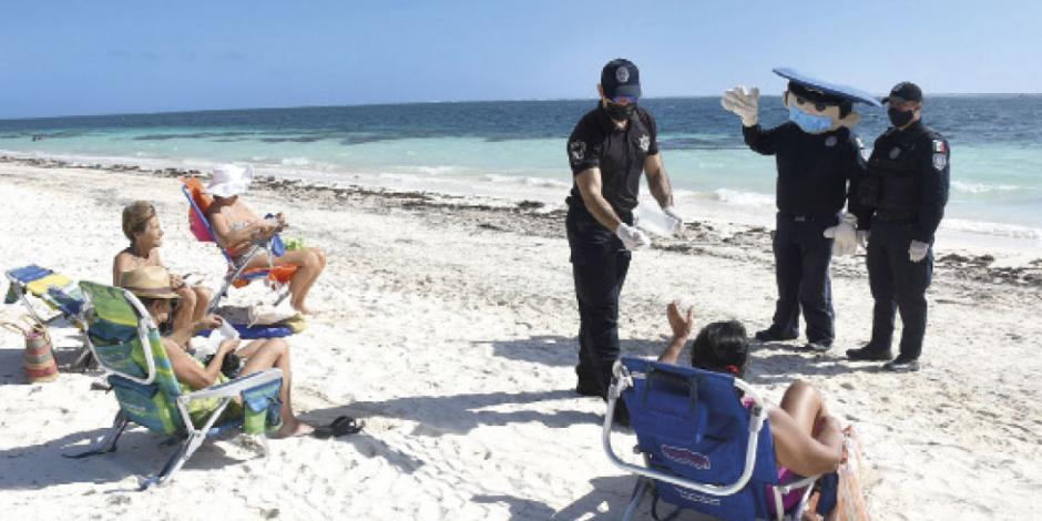 Un policía entrega mascarillas a turistas que no las portan a fin de evitar contagios
