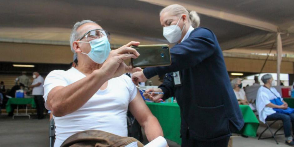 Persona mayor recibe la vacuna contra COVID-19, mientras se toma una "selfie" .