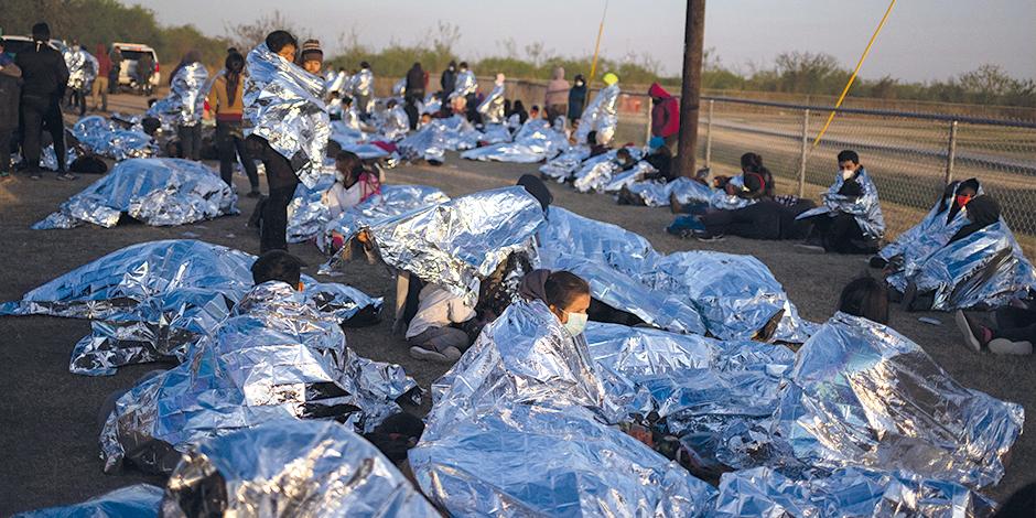 Decenas de migrantes se refugian en un campo de beisbol en espera de apoyo tras cruzar la frontera.