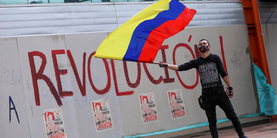 Un hombre ondea la bandera colombiana frente a un grafiti que dice "Revolución" durante una protesta que exige medidas gubernamentales para abordar la pobreza, la violencia policial y las desigualdades en los sistemas de salud y educación, en Bogotá, Colombia