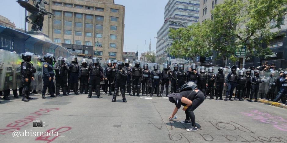 Una feminista realiza una pinta en el piso frente a policías capitalinos equipados con escudos antimotines.