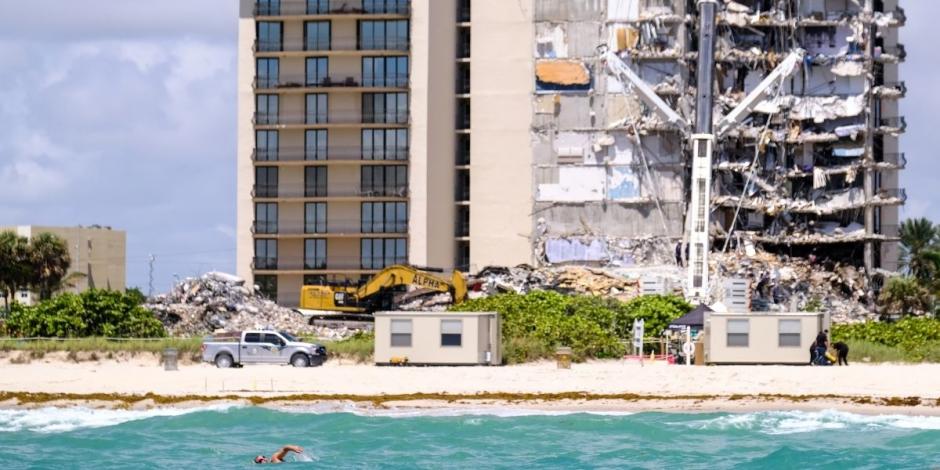 Un persona pasa nadando mientras el rescatistas continúan buscando víctimas días después de que un edificio residencial colapsara parcialmente en Surfside, cerca de Miami Beach, Florida,