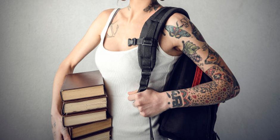 Una estudiante con tatuajes sostiene libros y mochila.