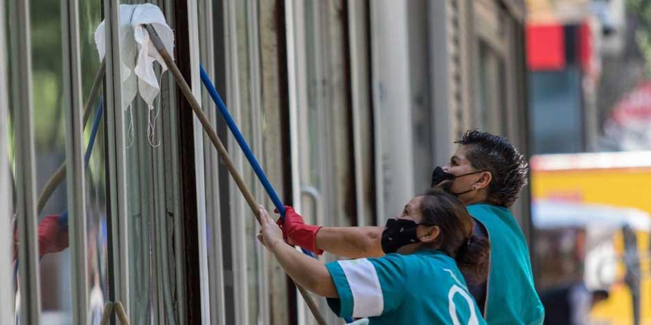 Un par de mujeres trabajan limpiando los cristales de un edificio en Paseo de la Reforma