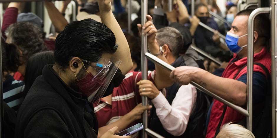 Un joven con cubrebocas y careta mira su celular en el Metro de la CDMX