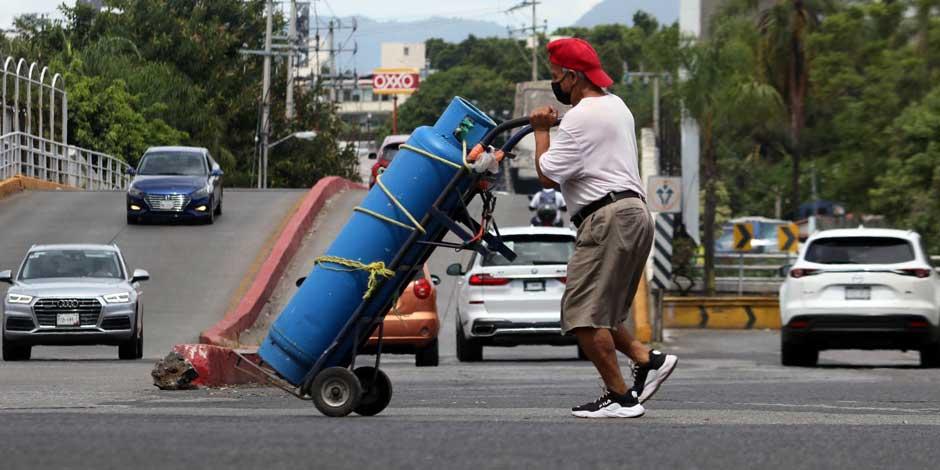 Un hombre transporta un tanque de gas con su diablito de carga por la calle