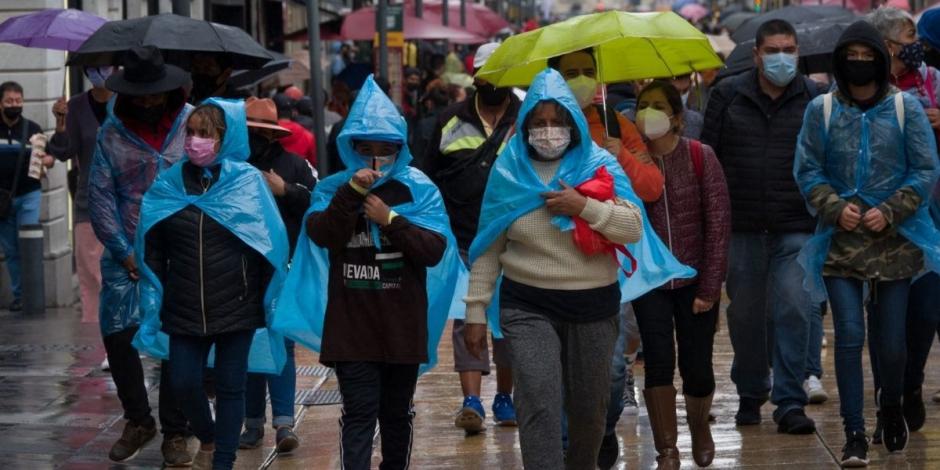 Personas portan impermeables y paraguas ante las lluvias en la Ciudad de México.