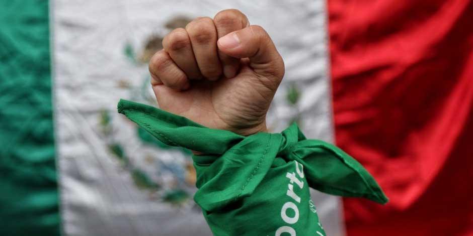 En la imagen, una mujer posa con pañuelo verde, símbolo del aborto legal, frente a una bandera de México durante el dictamen correspondiente de la SCJN