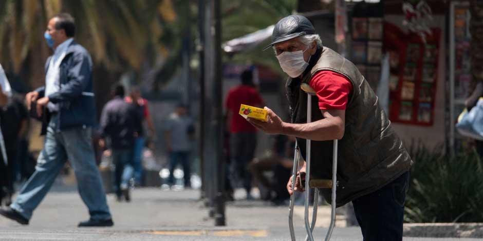 Una personas de la tercera edad vende mazapanes en la calle, protegido con un cubrebocas espera ganar algunas monedas para su sustento diario