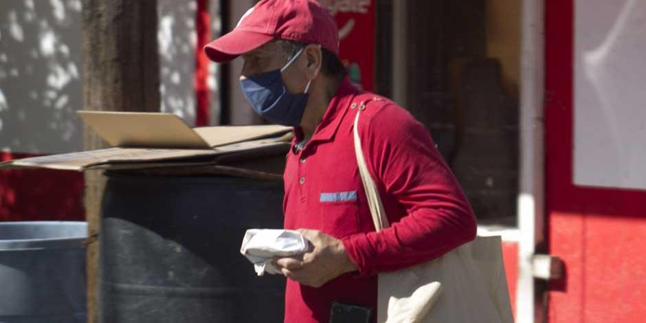 COVID-19: Un hombre con un paquete de tortillas en la mano y una bolsa en el brazo utiliza cubrebocas mientras anda en la calle para protegerse del coronavirus