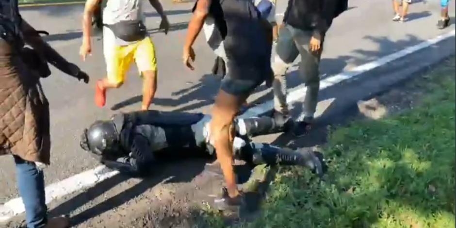 El video muestra al elemento de la Guardia Nacional cubrirse la cabeza, mientras los migrantes le quitan su equipo.