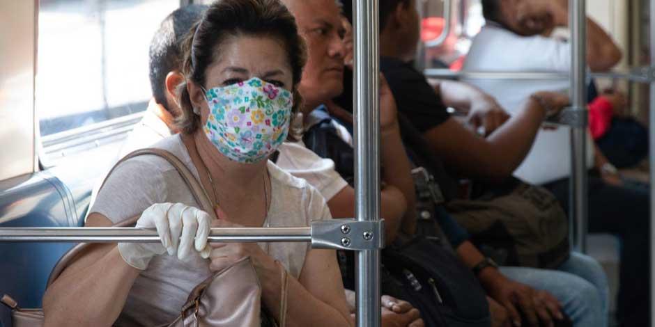 Una mujer en el transporte público se protege del COVID-19 con guantes y cubrebocas