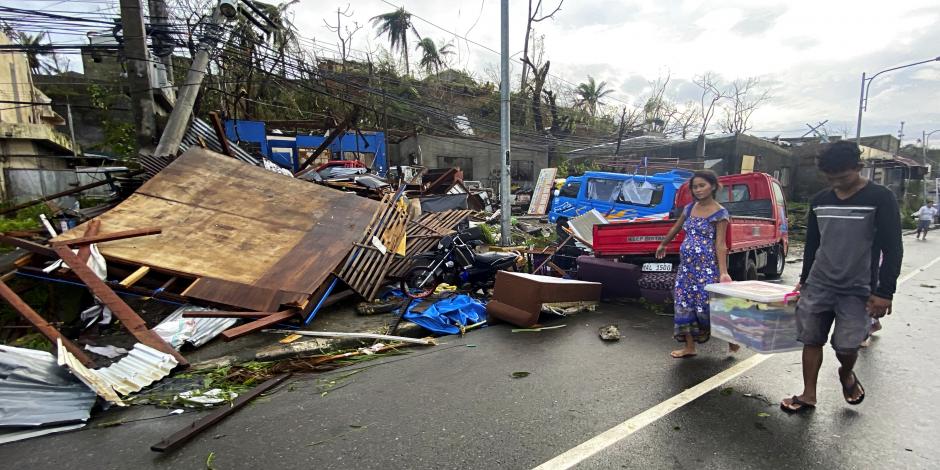 Residentes cargan con lo que queda de sus pertenencias mientras caminan frente a las casas dañadas por el tifón Rai en la ciudad de Surigao, en el centro de Filipinas.