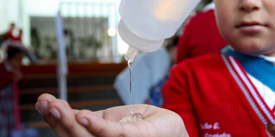 A un niño con uniforme escolar le ponen gel antibacterial en la mano para protegerse del coronavirus
