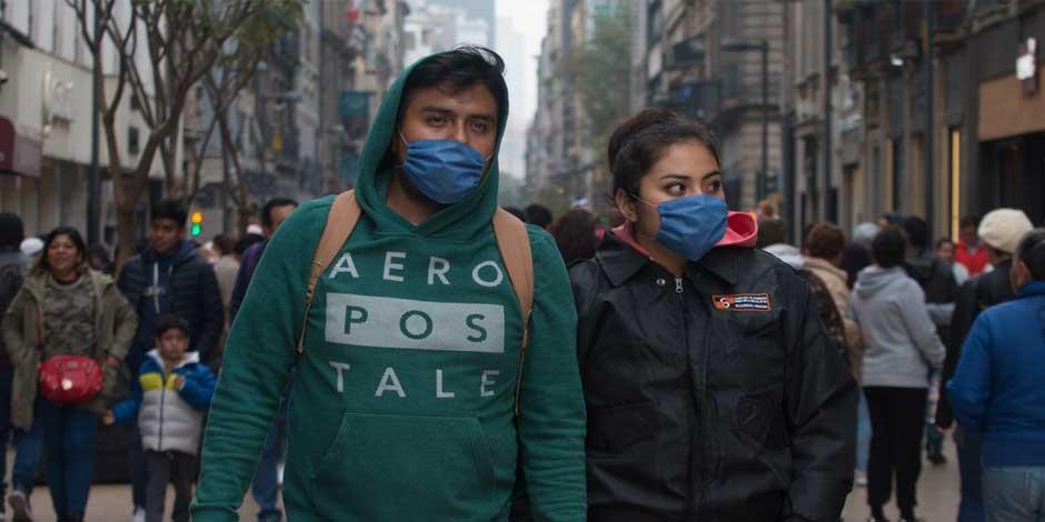 Una pareja camina por la calle con cubrebocas y ropa que los protege del frío