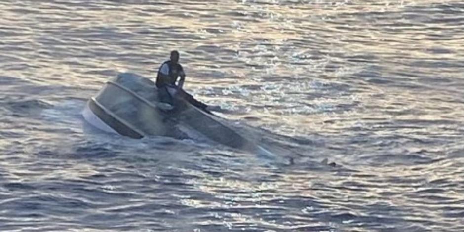 Un hombre, que dice ser una de las 40 personas que abandonaron Bimini, Bahamas, el sábado antes de encontrarse con un clima severo, se sienta en un bote volcado frente a las costas de Florida.