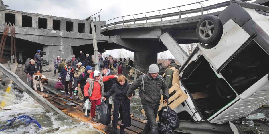 Familias cruzan, ayer, un camino improvisado debajo de un puente destruido, mientras huyen de Irpin, cerca de Kiev.