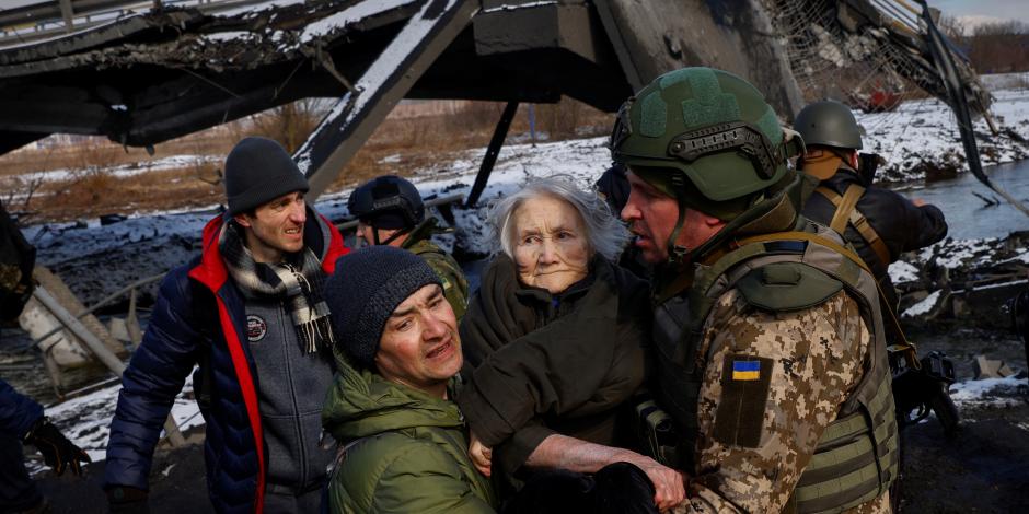 Dos hombres cargan a una mujer mientras la gente huye del avance de las tropas rusas cuyo ataque contra Ucrania continúa en la ciudad de Irpin, en las afueras de Kiev.